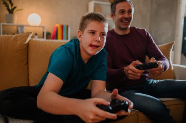 Babasıyla oynadığı video oyununa odaklanan mutlu bir gencin yakın çekimi. Babası arka planda gülüp eğlenirken o çok konsantre olup oyunu kazanmak istiyor..