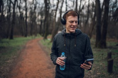 Kızıl saçlı atlet antrenmanına ara veriyor ve ormanda antrenman yaparken akıllı telefon kullanıyor. Sağlıklı yaşam tarzı kavramı.