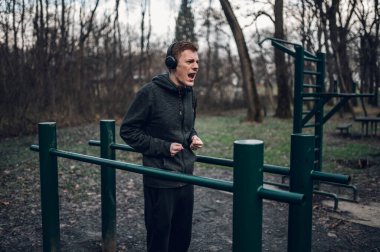 Kızıl saçlı sporcu ormanda spor ceket giyerek ve kulaklık takarak antrenman yapıyor. Sağlıklı yaşam tarzı konsepti.