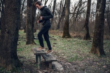 Kızıl saçlı sporcu ormanda spor ceket giyerek ve kulaklık takarak antrenman yapıyor. Sağlıklı yaşam tarzı konsepti.