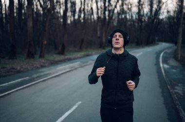 Atletik kızıl saçlı genç adam dağ yolunda koşuyor. Koşarken kulaklıkla müzik dinlemek. Atletik ve sağlıklı..