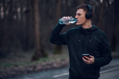 Genç kızıl saçlı adam doğada koşarken akıllı telefon ve kulaklık kullanıyor. Spor ve spor konsepti, sağlıklı yaşam tarzı, motivasyon..