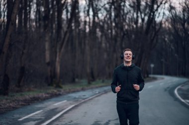 Atletik kızıl saçlı genç adam dağ yolunda koşuyor. Koşarken kulaklıkla müzik dinlemek. Atletik ve sağlıklı..