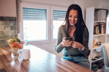 Çekici, orta yaşlı bir kadın sabah kahvesini içip evinde dinlenirken akıllı telefon kullanıyor. Rahatla, sessizlik, sabah ve yeni gün konseptine başla..