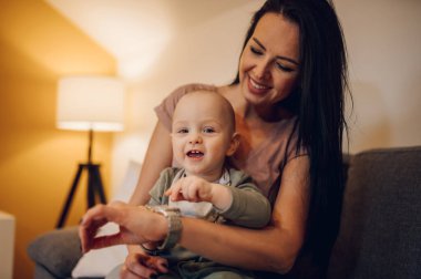 Küçük oğluyla kanepede vakit geçiren mutlu genç bir anne. Aile, bebek ve annelik kavramı. Anne oğul kaynaşıyor..