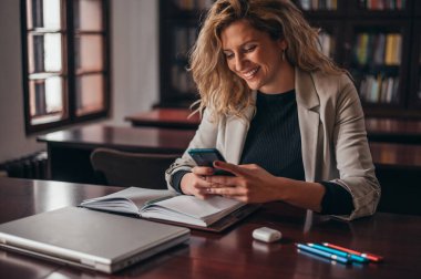 Ofisinde çalışırken akıllı telefon kullanan genç ve güzel bir iş kadını.