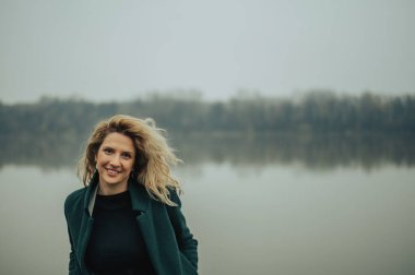 Nehrin kenarında yeşil ceketli genç sarışın kadın.