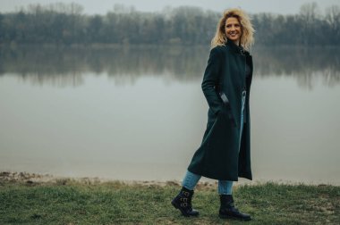 Nehrin kenarında yeşil ceketli genç sarışın kadın.