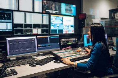 Televizyon yayın odasında orta yaşlı bir kadın TV editörü vizyon karıştırıcı ile çalışıyor. Stüdyoda editör. Televizyon stüdyosunda vizyon karıştırma paneli.