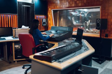 Orta yaşlı kadın müzik yapımcısı ses stüdyosundayken miksaj stüdyosunda çalışıyor. Stüdyo kontrol masası kaydediliyor. Profesyonel müzik stüdyosu.