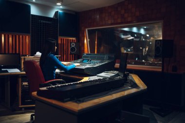 Orta yaşlı bir kadın müzik düzenleyicisi dijital kayıt stüdyosundaki bir ses ekipmanında şarkı yazıyor. Müzik yapımcısı. Ses mühendisi. Ses kayıt stüdyosunda ses operatörü.