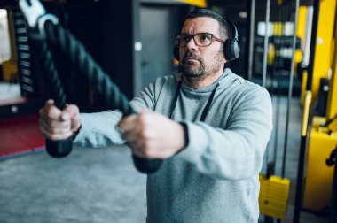 Spor salonunda antrenman yaparken çapraz makine kullanan orta yaşlı adamlar. Çapraz antrenman. Kilo vermeye çalışan şişman adam..