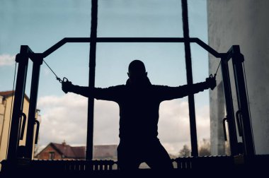 Spor salonunda antrenman yaparken çapraz makine kullanan bir adamın silüeti. Çapraz antrenman. Fitness yaşam tarzı.