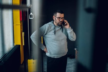 Kilolu orta yaşlı bir adam akıllı telefon kullanıyor ve spor salonunda antrenman yaparken mola veriyor. İş devam ediyor..