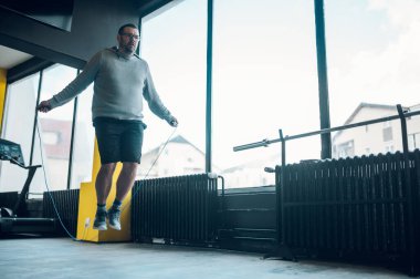 Spor salonunda antrenman yaparken ip atlayan şişman orta yaşlı bir adam. Kilo vermeye çalışan şişman bir adam. Sağlıklı yaşam tarzı.