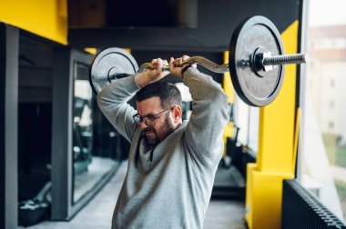 Spor salonunda antrenman yaparken halter kaldıran orta yaşlı bir adam. Kilo vermeye çalışan şişman bir adam. Sağlıklı yaşam tarzı.