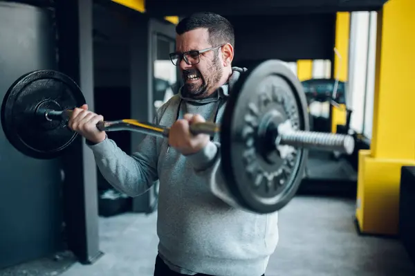 Spor salonundaki şişman, orta yaşlı adam halter kaldırma egzersizleri yapıyor. Sağlıklı yaşam tarzı kavramı. Fazla kilolu.