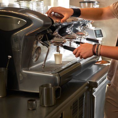 Espresso yapan bir kahve makinesinin yakın çekimi. Kahve, kahve makinesinin metal ağzının altındaki kağıt bardağa akıyor. Tek kullanımlık konteynerlerde sıcak kahve üretimi.