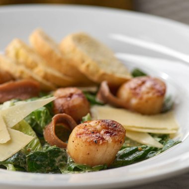 Zarif restoran beyaz arka plan üzerinde izole plaka üzerinde beyaz soslu kızarmış deniz tarak. Gurme istiridye et taze marul ile yakın bırakır