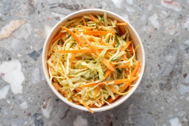 Kasede taze lahana salatası ve gri taştan arka plan manzarası. Partiler için yiyecek kavramı. Fast Food. Sağlıklı öğle yemeği. Tek kullanımlık kağıt tabakta yiyecek teslimatı. Çevre dostu karton paketleme