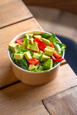 Avokado ve taze domates salatası kasede, üst manzara. Partiler için yiyecek kavramı. Fast Food. Sağlıklı öğle yemeği. Tek kullanımlık kağıt tabakta yiyecek teslimatı. Çevre dostu karton paketleme ortamı