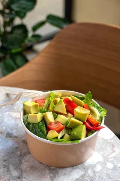 Avocado and fresh tomatoes salad in bowl on gray stone background top view. Concept Food For Parties. Fast Food. Healthy lunch. Food delivery in disposable plate of craft paper. Eco-friendly carton packaging environment protection