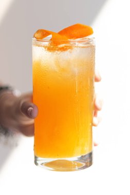 Soğuk yaz kokteyli dişinin elinde, yakın plan. Bir kadının eli, yaz kafesinde limon ve buzla serinletici bir kokteylin sisli bardağını tutuyor..