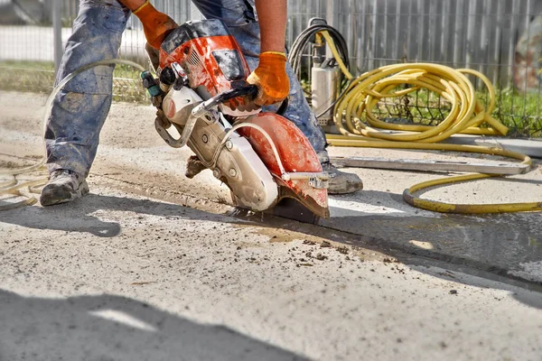 Construction worker cutting concrete foundation using a cut-off saw. Profile on the blade of an asphalt or concrete cutter with workers shoes and protective gear.