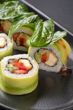 Siyah pirinç, avokado ve beyaz tabakta tatlı patatesli vejetaryen suşisi. Vegan gıda konsepti. Sebzeli vejetaryen suşi ve siyah tabakta avokado dilimi. sağlıklı renkli gıda geçmişi.