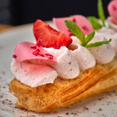 Beyaz tabakta kremalı ve çilekli ekler. Masaya yakın çekim, bir restoranda servis, menü yemek konsepti.