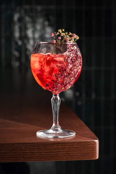 delicious light red cocktail in Tall glass of gin tonic filled with ice and Red flowers for decoration, dark background, vertical, side view.