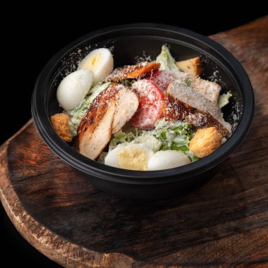 Sezar salatası. Yuvarlak siyah beslenme çantasında salata, tepside yemek, fotokopi alanı, menü ve reklam için yemek. yakın plan