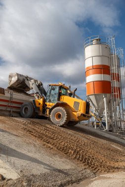 Ön yükleyici ezilmiş taşı makine betonuna boşaltıyor. Yapım odasının arka planına karşı. Ağır ekipman.