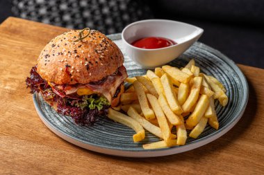 Çedar peynirli sığır pirzolası, pastırma dilimleri, domates ve turşulu hamburgerle susamlı beyaz çörek. Lezzetli. Restoranda servis edilen yemek, menü yemek konsepti..