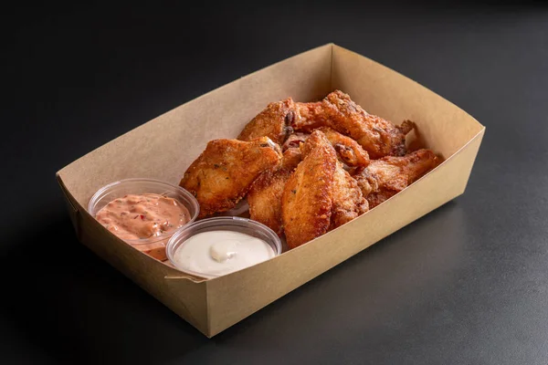 Fried chicken wings in a paper box on a dark background. Snacks in a paper box. Deep chicken wings or appetizer, fast food. Dish of crisp golden chips.