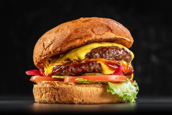 Delicious double cheeseburger with American cheese, lettuce, tomato, red onion, pickles, and farmhouse bun close up on a black background. Delicious cheeseburger. sandwich fast food, amazing food