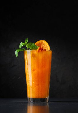 Siyah arka planda uzun bir bardakta deniz dikenli çilek, narenciye ve baharatla meyveli punç. Yaratıcı minimalist kavram. Karanlık bir taş arka planda.