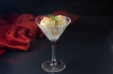 Ballı ve fındıklı kremalı dondurma, martini bardağında çıtır çıtır fındıklı ve siyah arka planda naneli. Yaratıcı minimalist kavram. Karanlık bir taş arka planda.