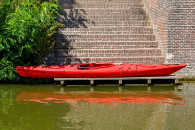 Kanalın kenarındaki merdivenlerin altındaki ahşap iskelede kırmızı plastik bir kano. Kimse yok..