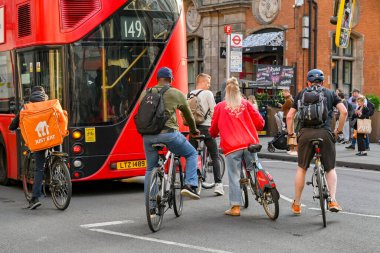 Londra, İngiltere, İngiltere - Haziran 2022: Londra şehir merkezindeki bir caddede kırmızı bir Londra otobüsünün arkasında bekleyen bisikletçiler