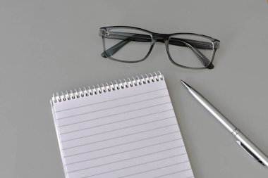 Açık gri arka planda düz bir defter, kalem ve bir çift gözlük. Boşluğu kopyala.