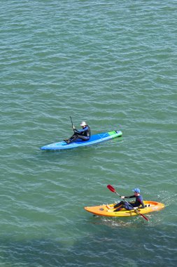 Newport, Pembrokeshire, Galler - Ağustos 2022: İki kişi sakin bir denizde plastik kano sürüyor