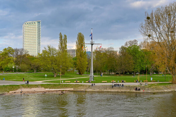 Mannheim, Germany - April 2022: People in one of the city's public parks alongside the Schiffermast am Rhein or Fahnenmast sculpture, which is a tourist attraction