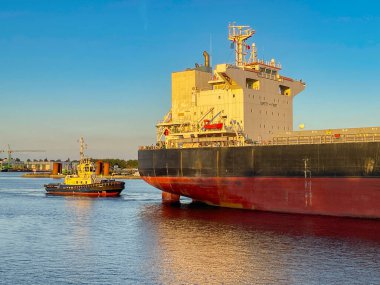 Amsterdam, Netherlands - August 2022: Tug boat assisting a large cargo ship Imbari Queen as it docks in one of the city's harbours