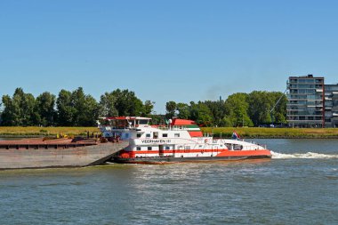 Dordrecht, Netherlands - August 2022: Powerful tug pushing heavy industrial barges on the River Maas.