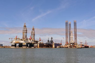 Galveston, Texas, USA - Febriuary 2023: Oil rigs in the city's port for maintenance and repair, with the historic USS Texas warship being restored in dry dock
