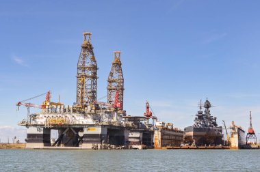 Galveston, Texas, USA - Febriuary 2023: Oil rigs in the city's port for maintenance and repair, with the historic USS Texas warship being restored in dry dock