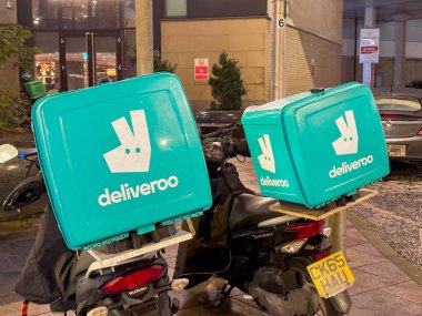 Cardiff, Wales - February 2023: Insulated containers used by the Deliveroo fast food delivery business on the back of motor scooters parked in a city street at night