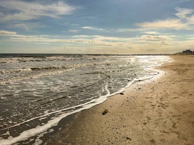 Water's edge of an incoming tide on the beach in Galveston, Texas, in evening sunlight. No people. clipart
