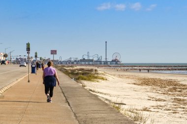 Galveston, Teksas, ABD - Şubat 2023: Arka planda kentin tarihi iskelesi boyunca yürüyen kişi